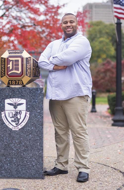 Veteran Jeffrey Brown standing next to the DU ring with a red leaved tree and American flag in the background.